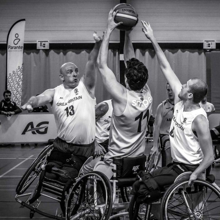 Mark playing wheelchair basketball on tilt stopping a dutch player from shooting, while Kyle March tries to intercept the ball