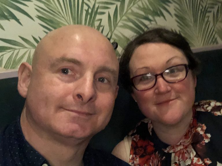 Mark and wife smiling together in a floral-themed interior.